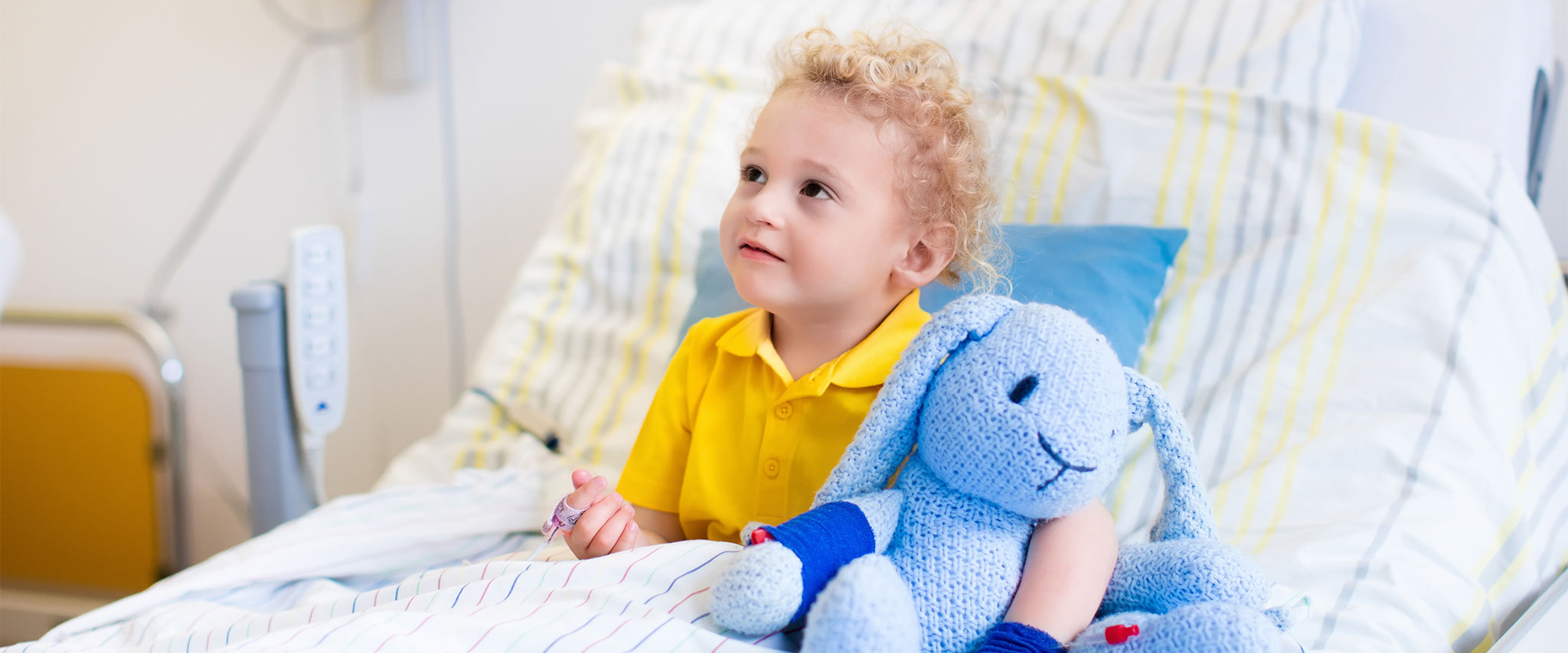 Kind im Krankenbett mit Kuscheltier und Anschluss an Geräte