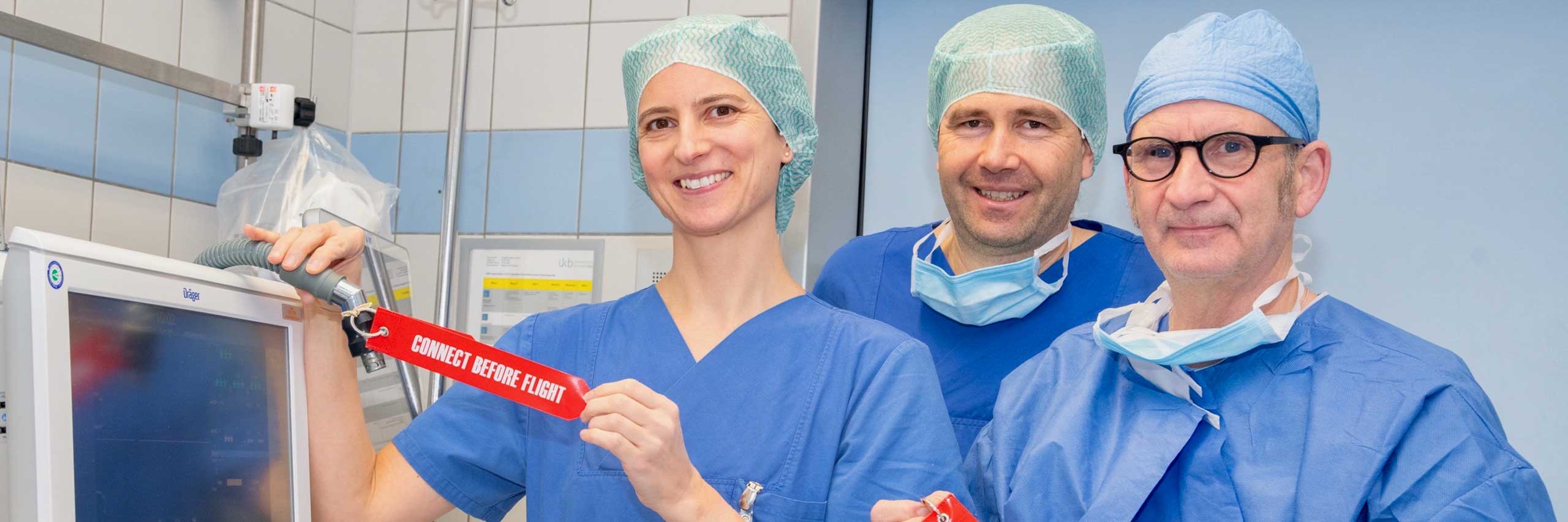 Dr. Christina Weisheit, Oberärztin der Klinik für Anästhesiologie und Operative Intensivmedizin; Prof. Mark Coburn, Direktor der Klinik für Anästhesiologie und Operative Intensivmedizin; und Rainer Ebert, Anästhesie-Pflegekraft sehen Anhänger "Connect Before Flight" als eine Kombination aus visuellem Hinweis, Routinebildung, Verantwortungsgefühl und Engagement für die Pausierung der Narkosegasabsaugung.